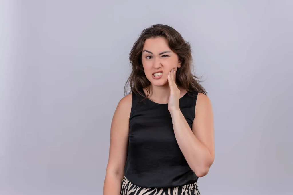 Woman showing teeth sore after cleaning with hand on cheek.