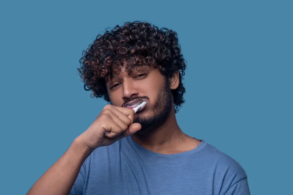 Man brushing his teeth with discomfort because his teeth hurt after cleaning